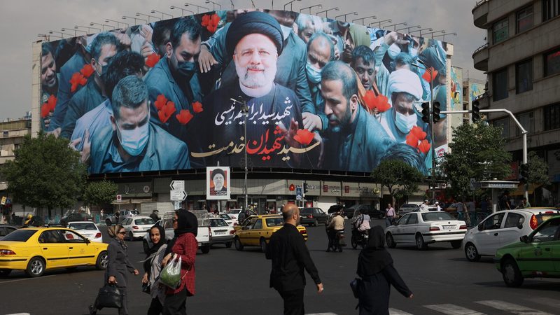 People in Tehran walk past a billboard paying tribute to President Ebrahim Raisi, who died in a helicopter crash last weekend