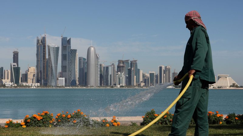 Gardener watering plants on the Corniche with West Bay skyline of Doha in the background.