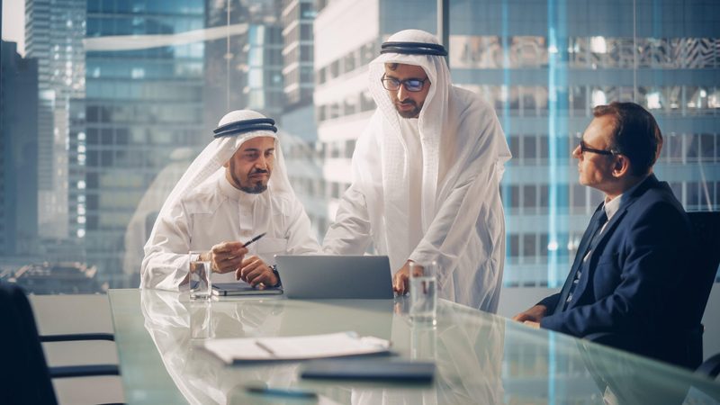 International Business Consultant Advises on Financial Strategy Plan to Successful Arab Company Owners. Multicultural Meeting in Modern Office Between American and Saudi Businessman