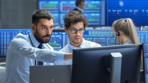 M79HAK Professional Broker Consults Stock Exchange Trader at His Workstation. Multi-Ethnic Team at Stock Exchange Office is Busy Selling and Buying Stocks