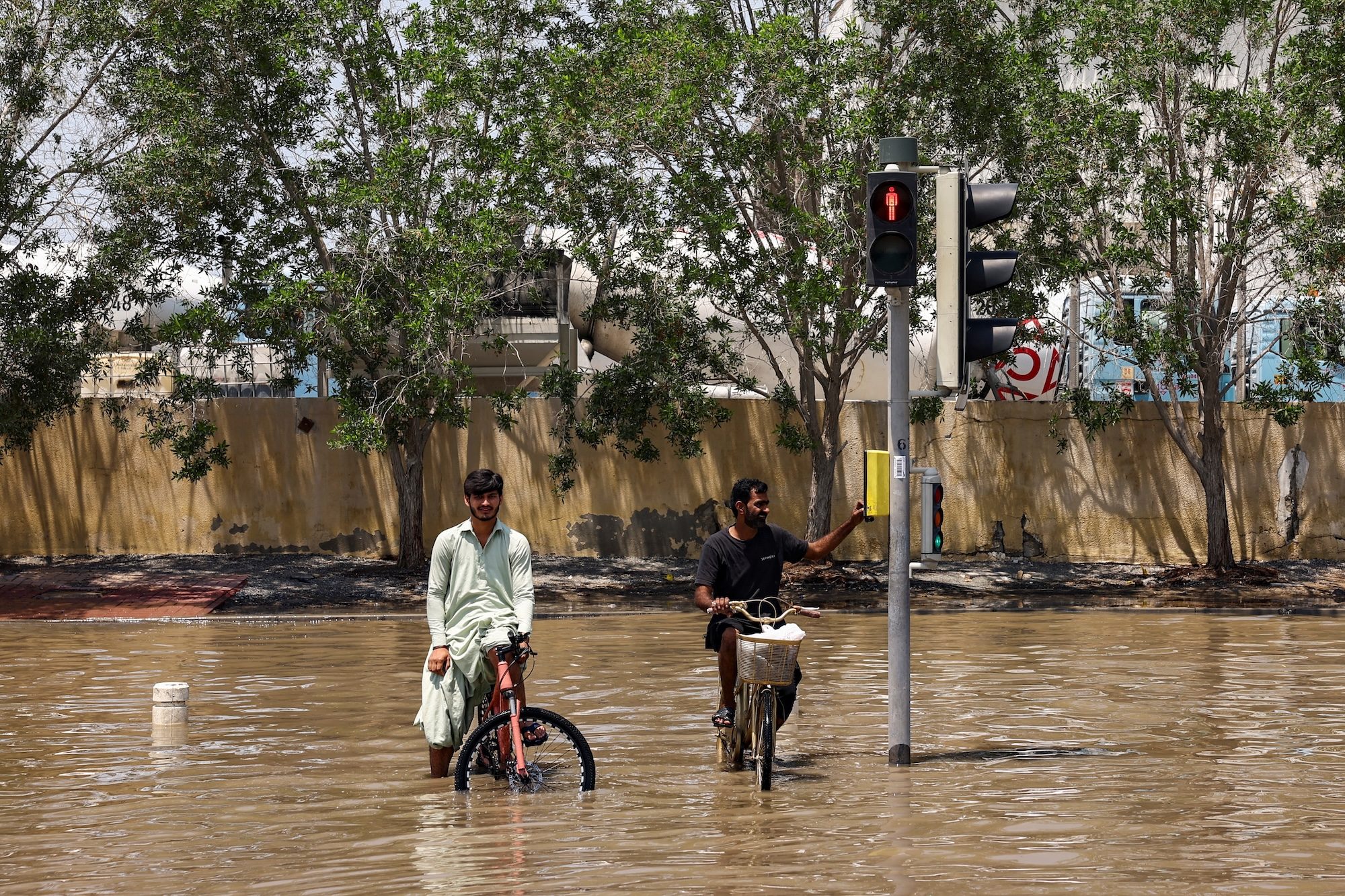 People sitting on bicycles look on amidst flood water following heavy rainfall, in Dubai, United Arab Emirates, April 19, 2024