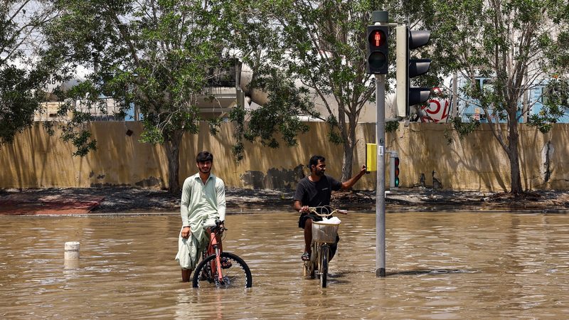 People sitting on bicycles look on amidst flood water following heavy rainfall, in Dubai, United Arab Emirates, April 19, 2024