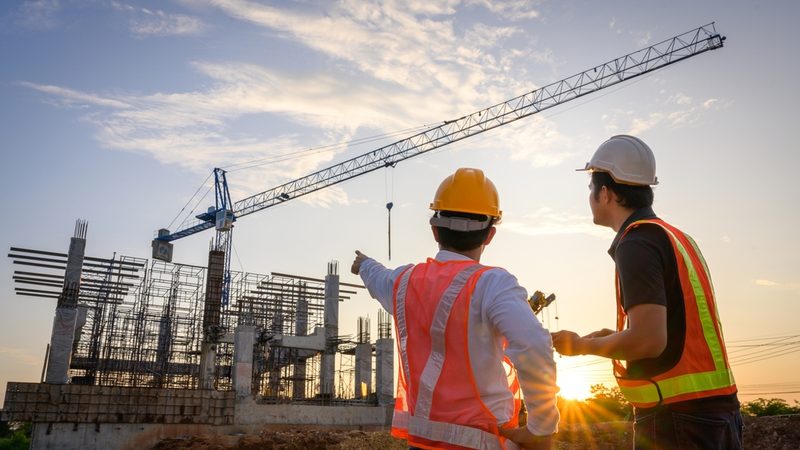 Two men in high-vis outfits and hard hats at a construction site.