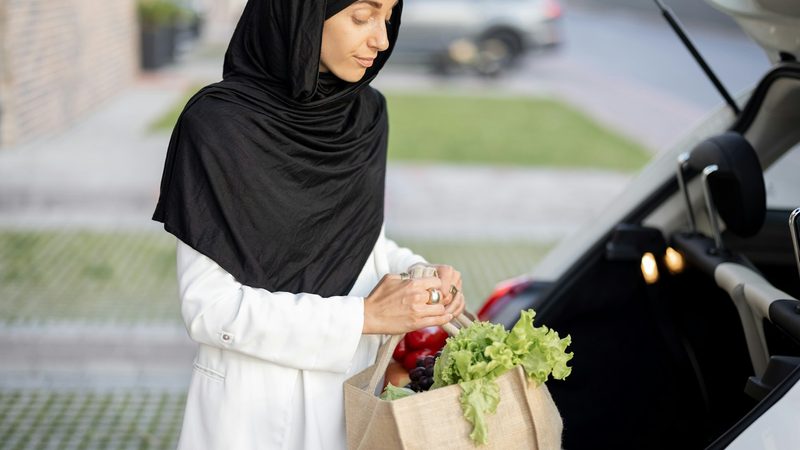 A woman in a headscarf loads groceries into the back of a car. Saudi consumer spending rose as shoppers stocked up ahead of Ramadan